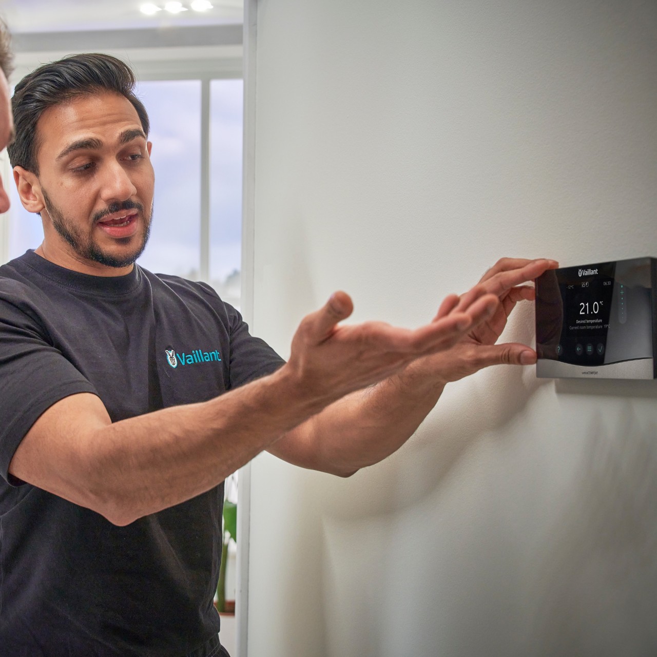 man showing a homeowner a heating control on the wall