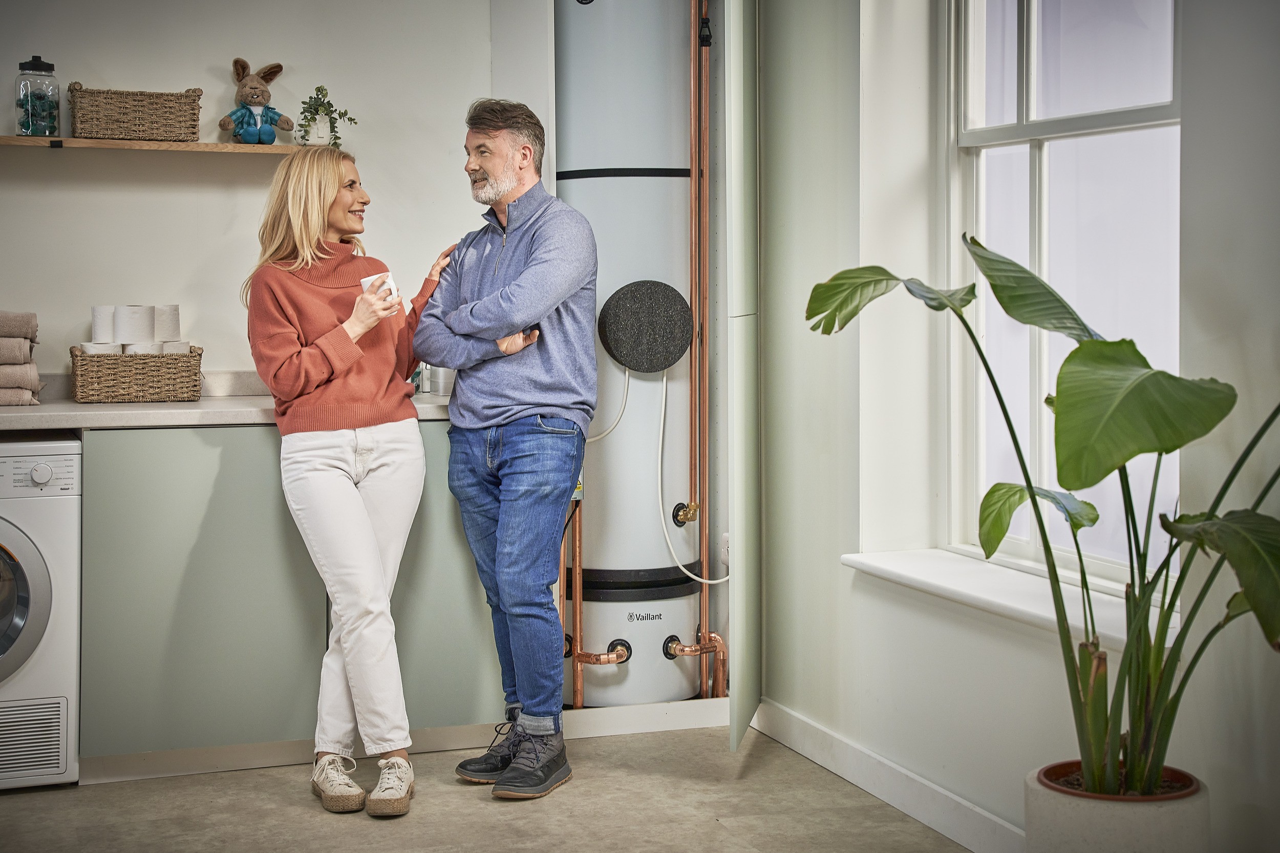 A man and woman are positioned in front of a cylindrical water heater, engaged in conversation about its operation.