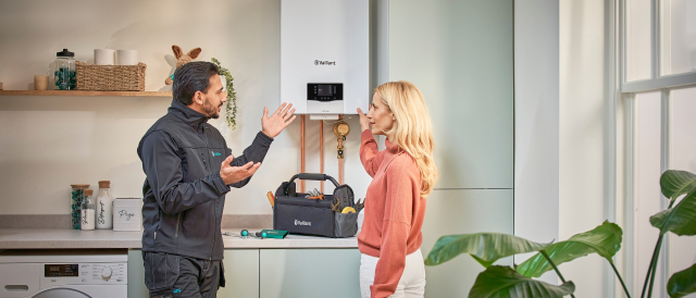 An installer speaking to a woman in front of a Vaillant boiler in a kitchen. 