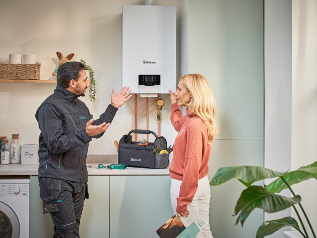 An installer speaking to a woman in front of a Vaillant boiler in a kitchen. 
